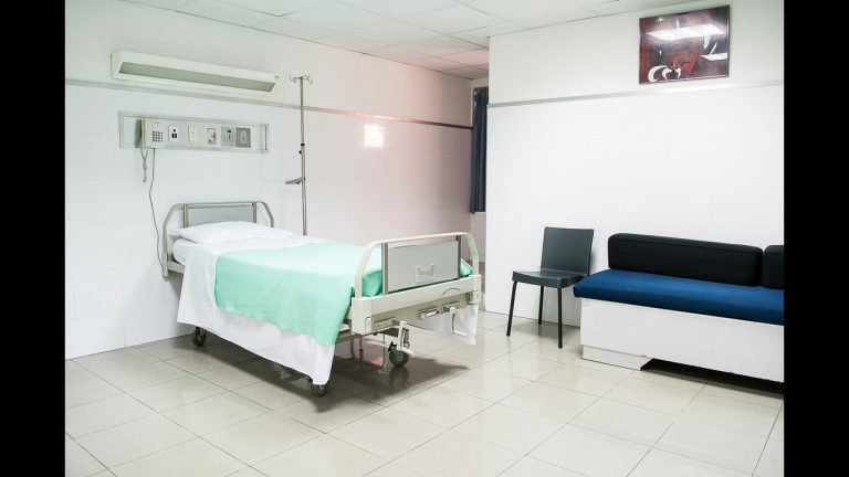 Empty hospital room with a light blue sheet on the bed and a small blue couch along the wall