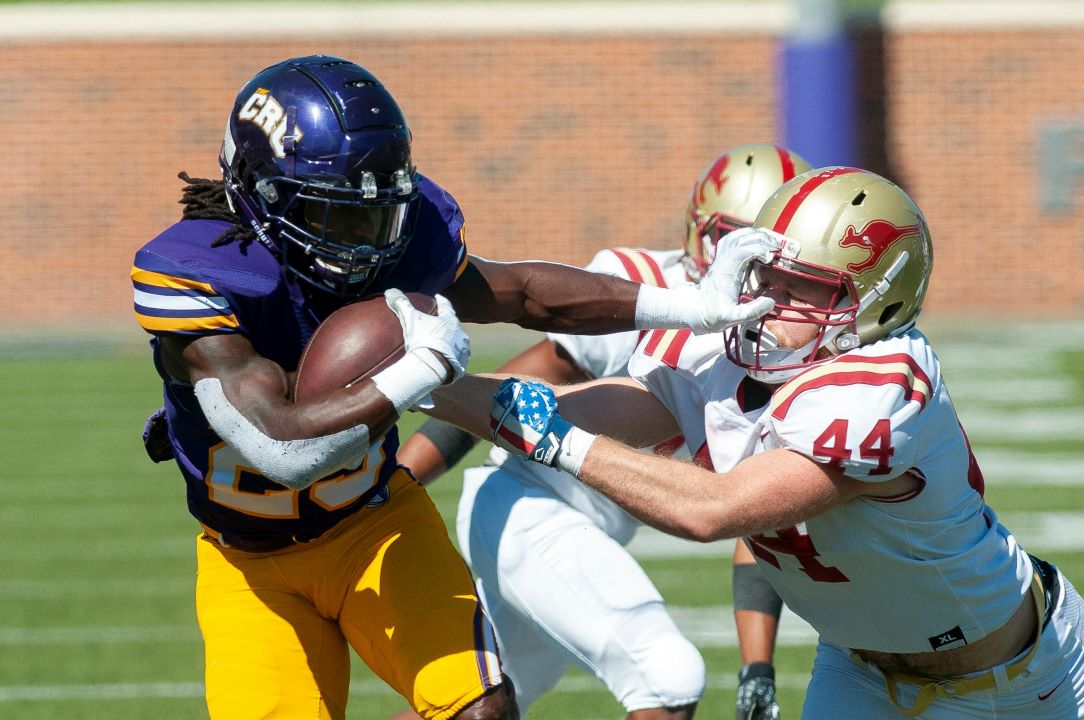 A football player carrying the ball and stiff-arming another player in the helmet.