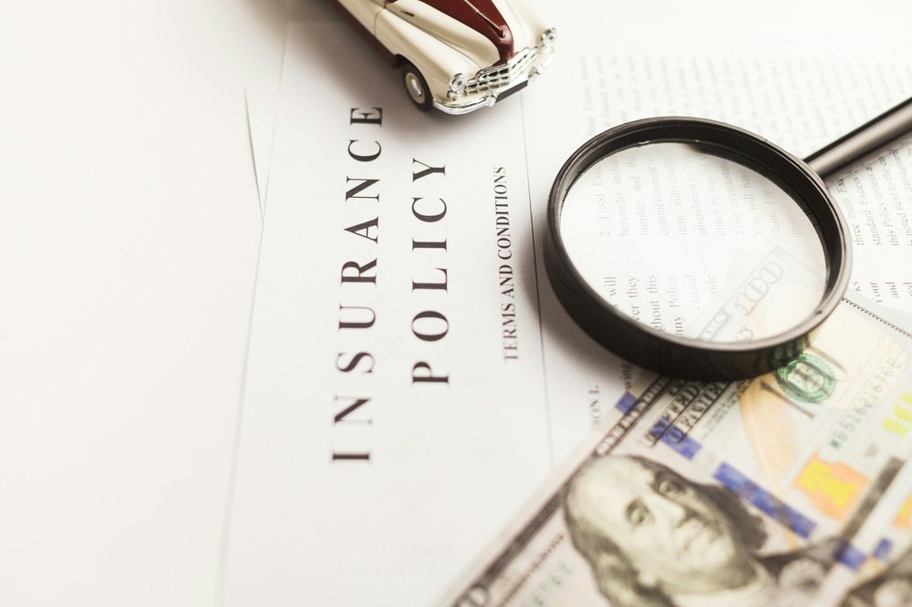 Paper which says "Insurance Policy" with a magnifying glass and 100-dollar bill on top