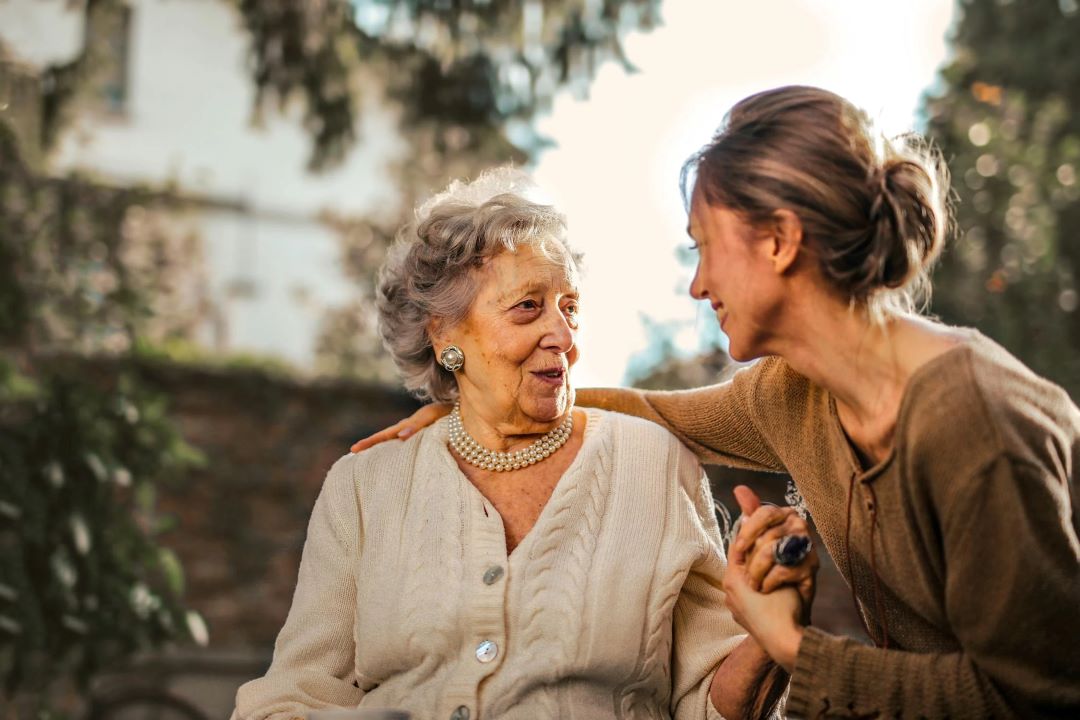 A younger woman embraces an older woman on a park bench